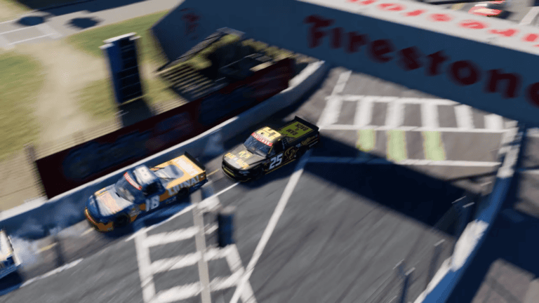 NASCAR 26 aerial camera angle showing two Truck Series trucks racing at a short track with Firestone branding visible on the track overpass structure