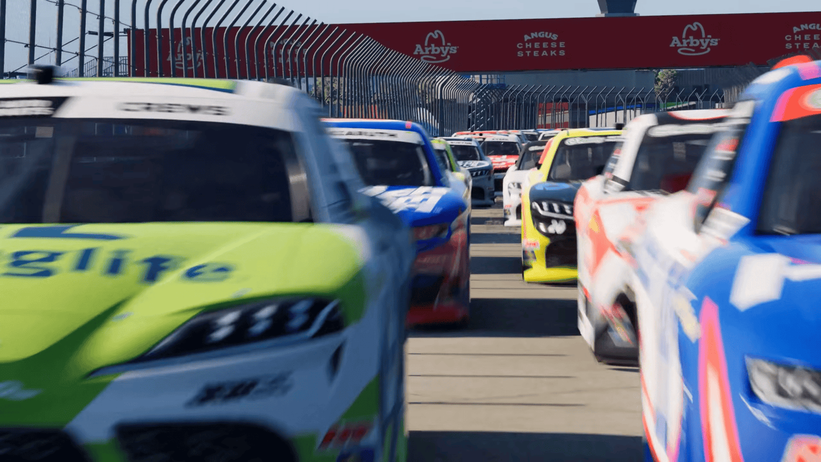 NASCAR 26 gameplay showing multiple cars lined up on pit road with an Arby's sponsor gantry overhead and packed pit lane